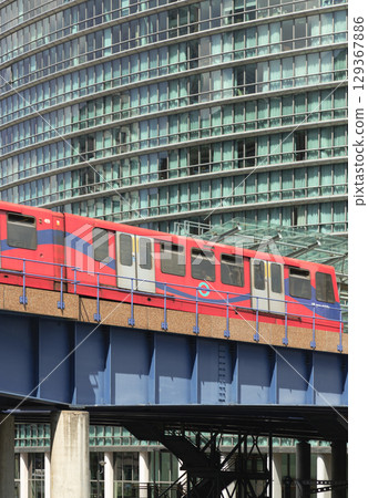 Docklands Light Railway (DLR) train on an elevated track with modern buildings in the background. 129367886