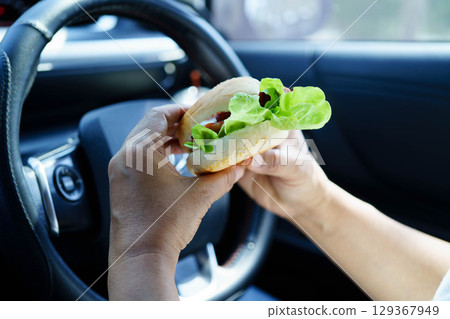 Asian woman driver hold and eat hamburger food in car. Asian woman driver hold and eat hamburger food in car. 129367949