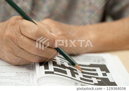elderly woman playing sudoku puzzle game. 129368036