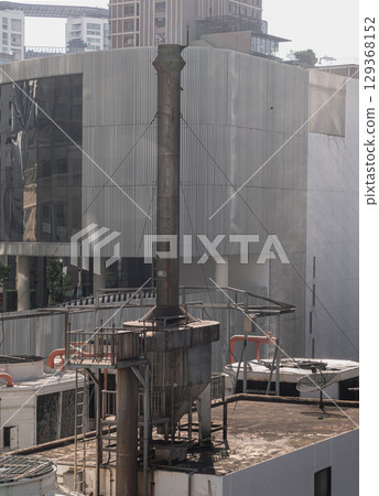 Boiler soot separator chimney on roof of building with modern buildings in the background. 129368152