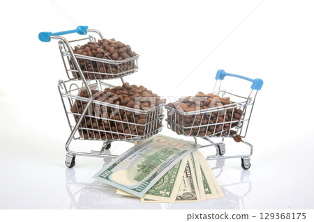 Tiny carts loaded with coffee beans alongside dollar bills, illustrating the concept of money Tiny carts loaded with coffee beans alongside dollar bills, illustrating the concept of money 129368175