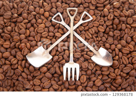Elegant still life featuring two crossed metal shovels surrounded by roasted coffee beans 129368178