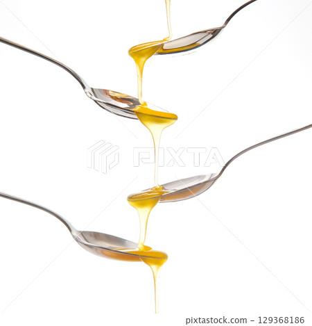 A striking image of golden honey cascading from one metal spoon  129368186