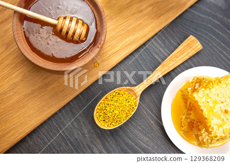 A rustic wooden table displays a bowl of golden honey with a wooden dipper, a plate of honeycomb 129368209