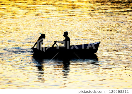 silhouette of people in boats with oars on the evening river silhouette of people in boats with oars on the evening river 129368211