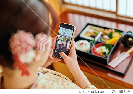 A woman in a kimono taking a photo with her smartphone 129368299