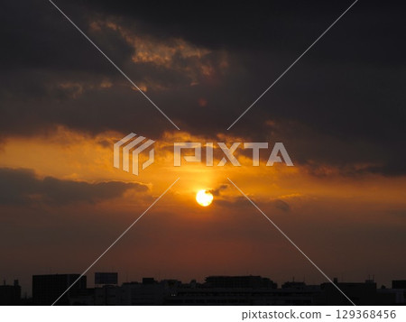 The setting sun peeking out from between the clouds 129368456