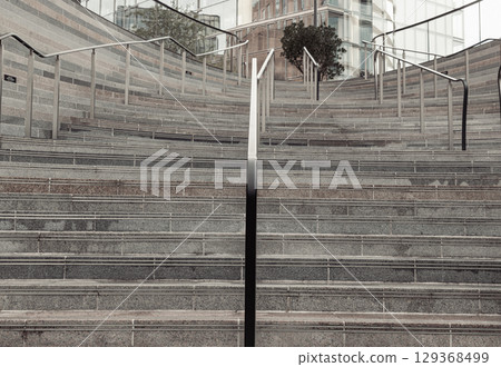 Perspective view of outdoor steps that become walls with stainless steel sleek railings handle grip of leading to entrance into modern building. Perspective view of outdoor steps that become walls with stainless steel sleek railings handle grip of leading to entrance into modern building. 129368499