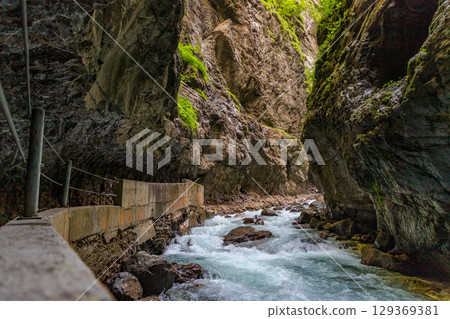 Narrow walkway carved into the cliffside along a turquoise stream inside Partnachklamm Gorge, Garmisch-Partenkirchen, Bavaria. A stunning natural passageway through dramatic alpine rock formations. 129369381