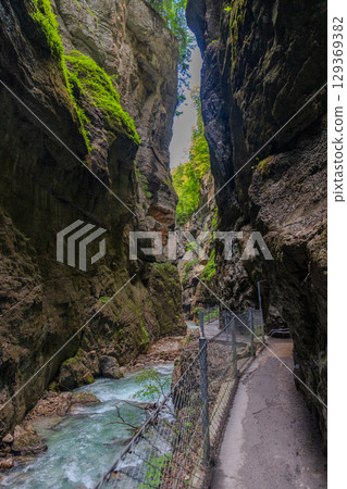 Narrow walkway carved into the cliffside along a turquoise stream inside Partnachklamm Gorge, Garmisch-Partenkirchen, Bavaria. A stunning natural passageway through dramatic alpine rock formations. 129369382