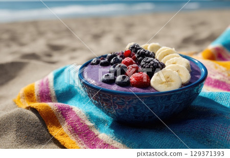 vibrant blue bowl filled with a purple smoothie, topped with banana slices and berries 129371393