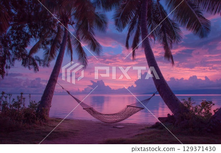 A cozy hammock between two palm trees on the beach at sunset, with a pink and purple sky. 129371430