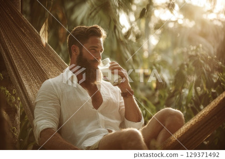 handsome man with a beard sitting in a hammock, drinking milk in a summer tropical environment 129371492