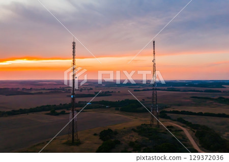 Two Communication Towers Against a Dusk Sky Over A Vast Rural Landscape at Sunset 129372036