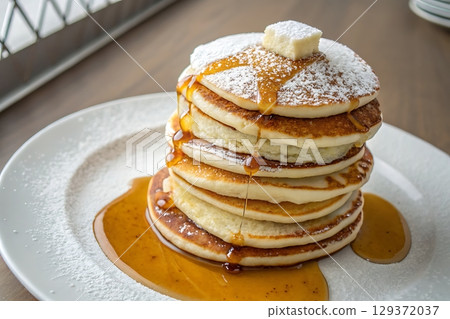 Stacked Fluffy Pancakes with Butter and Maple Syrup on a White Plate in a Cozy Cafe Setting Stacked Fluffy Pancakes with Butter and Maple Syrup on a White Plate in a Cozy Cafe Setting 129372037