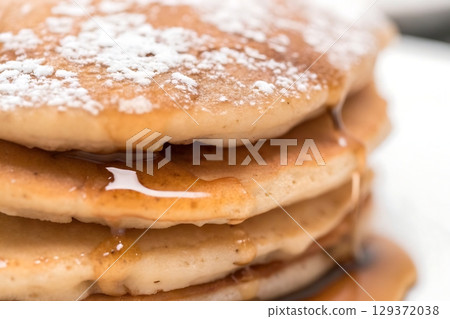Delicious fluffy pancakes stacked high with syrup and powdered sugar on a white plate 129372038