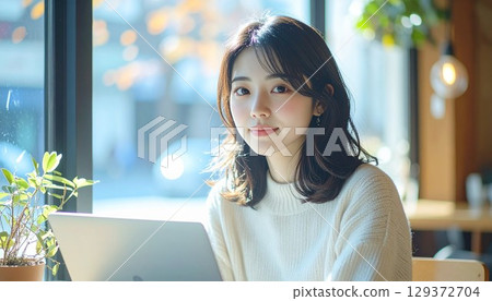 一位年輕的日本女性在明亮的咖啡館裡靠窗使用筆記型電腦 一位年輕的日本女性在明亮的咖啡館裡靠窗使用筆記型電腦 129372704