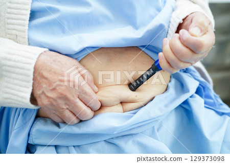 Asian senior woman making injection insulin pen in belly to treatment diabetes. 129373098