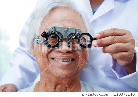 Optometrist checking Asian elderly woman ophthalmic vision eye test and using optical trial frame. Optometrist checking Asian elderly woman ophthalmic vision eye test and using optical trial frame. 129373110