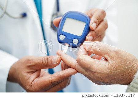 Asian doctor using digital glucose meter for check sample blood sugar level to treatment diabetes. Asian doctor using digital glucose meter for check sample blood sugar level to treatment diabetes. 129373117
