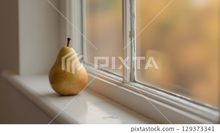 A single ripe pear sitting on a windowsill next to an obscured window with sunlight A single ripe pear sitting on a windowsill next to an obscured window with sunlight 129373341