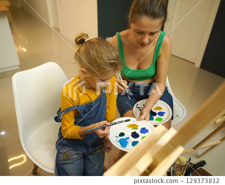 A mother and her daughter are engaged in a painting session  129373812