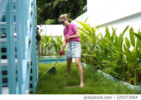 A woman raking the lawn at the backyard of her house  129373864