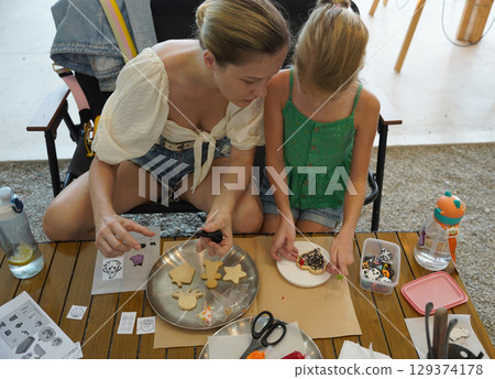 Mother and her daughter paint Halloween cookies  129374178