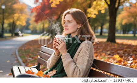 Young woman enjoying hot drink on bench in autumn park surrounded by colorful trees and fallen leaves 129374463