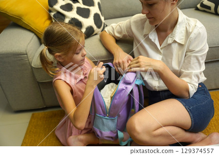 Mother helps her daughter pack her backpack  129374557