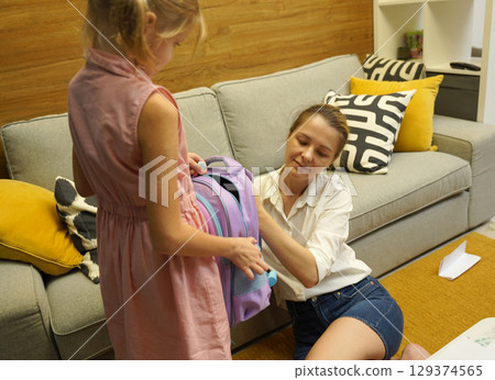 Mother helps her daughter pack her backpack  129374565