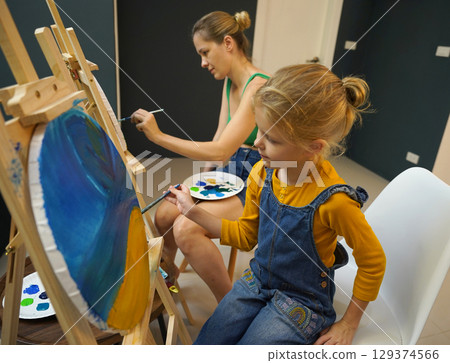 A mother and her daughter are engaged in a painting session  129374566
