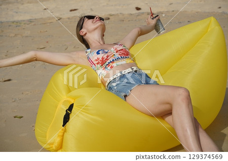 A young woman on the beach lounging on a yellow bean bag A young woman on the beach lounging on a yellow bean bag 129374569
