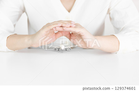 Hands Protecting White Airplane Model Symbolizing Travel Safety Hands Protecting White Airplane Model Symbolizing Travel Safety 129374601