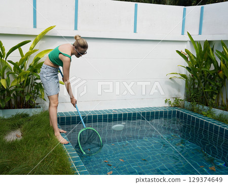 A young woman clean leaves out of a pool A young woman clean leaves out of a pool 129374649