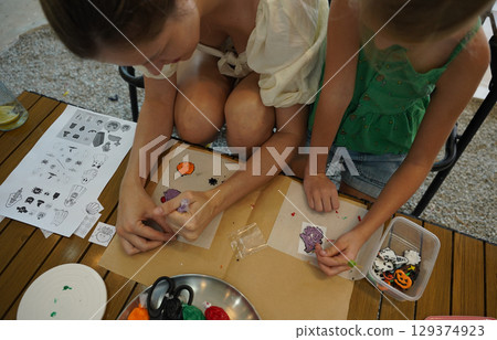 Mother and her daughter paint Halloween cookies  129374923