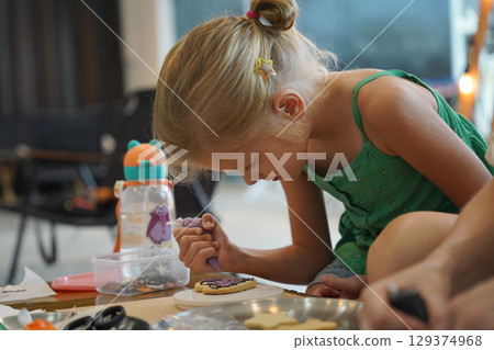 Mother and her daughter paint Halloween cookies  129374968