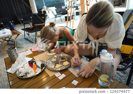 Mother and her daughter paint Halloween cookies  129374977