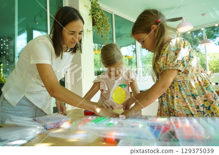 Teacher in workshop teched two girls how to assemble a thermo mosaic Teacher in workshop teched two girls how to assemble a thermo mosaic 129375039