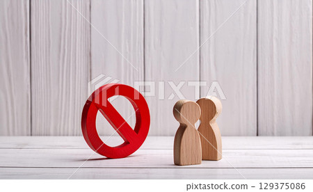 Two Wooden Figures Facing Red Forbidden Sign on White Wooden Background Symbolizing Restriction 129375086