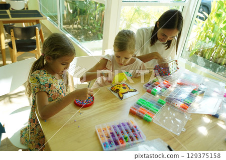 Teacher in workshop teched two girls how to assemble a thermo mosaic Teacher in workshop teched two girls how to assemble a thermo mosaic 129375158