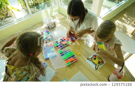 Teacher in workshop teched two girls how to assemble a thermo mosaic  129375188