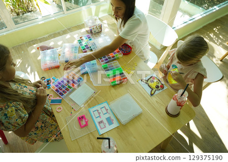 Teacher in workshop teched two girls how to assemble a thermo mosaic  129375190