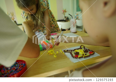 Teacher in workshop teched two girls how to assemble a thermo mosaic  129375193