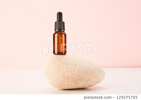 Glass amber vial on spa stone on pink background. 129375785