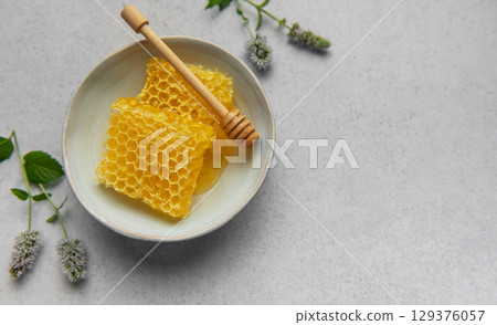 Honeycomb, honey dipper and fresh mint resting on a ceramic bowl 129376057