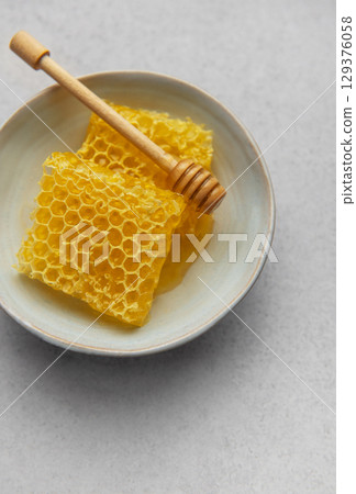 Honeycomb and honey dipper resting in ceramic bowl on table 129376058