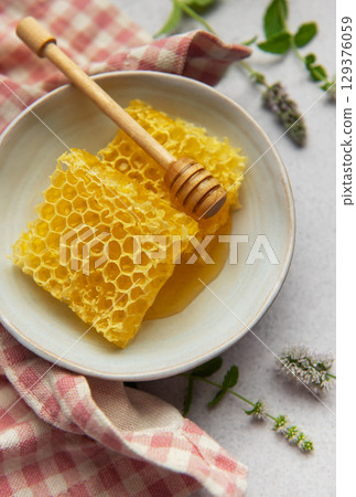 Honeycomb resting in bowl with honey dipper and fresh mint 129376059