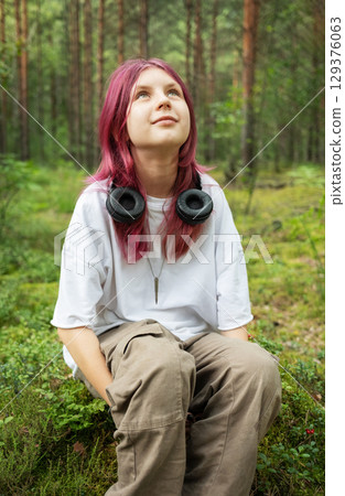Teenage girl with pink hair enjoying nature and music in forest 129376063