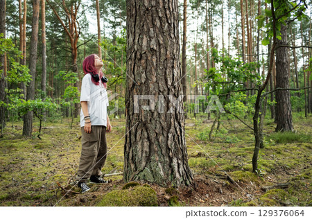 Youngster breathing fresh air in a lush forest by a large tree 129376064